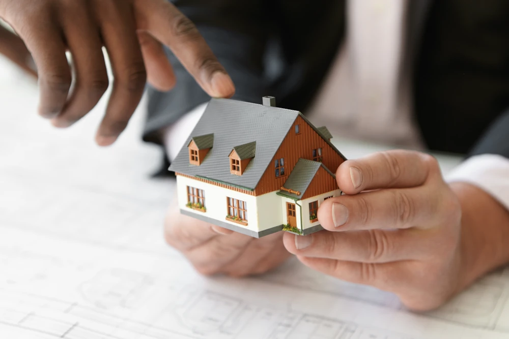 Contractor holding a home expansion project while his colleague points a finger to the scale model building, representing the importance of choosing Goveias as the contractor for your project.
