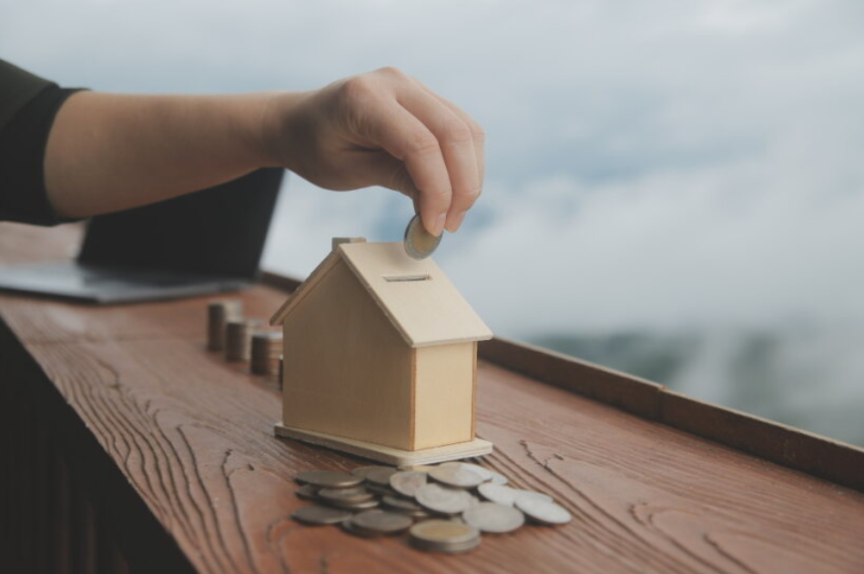 A woman puts coins into a wooden box in the shape of a house to renovate the house and increase the property’s value.