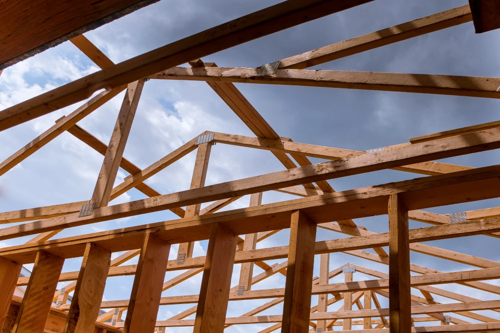 New construction beams at an angle where you can see the cloudy sky with sunlight, an example of a construction site for new builds and residential additions, representing home expansions.
