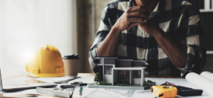 A construction worker sits at a table analyzing a renovation project, representing the importance of knowing how to flip houses.