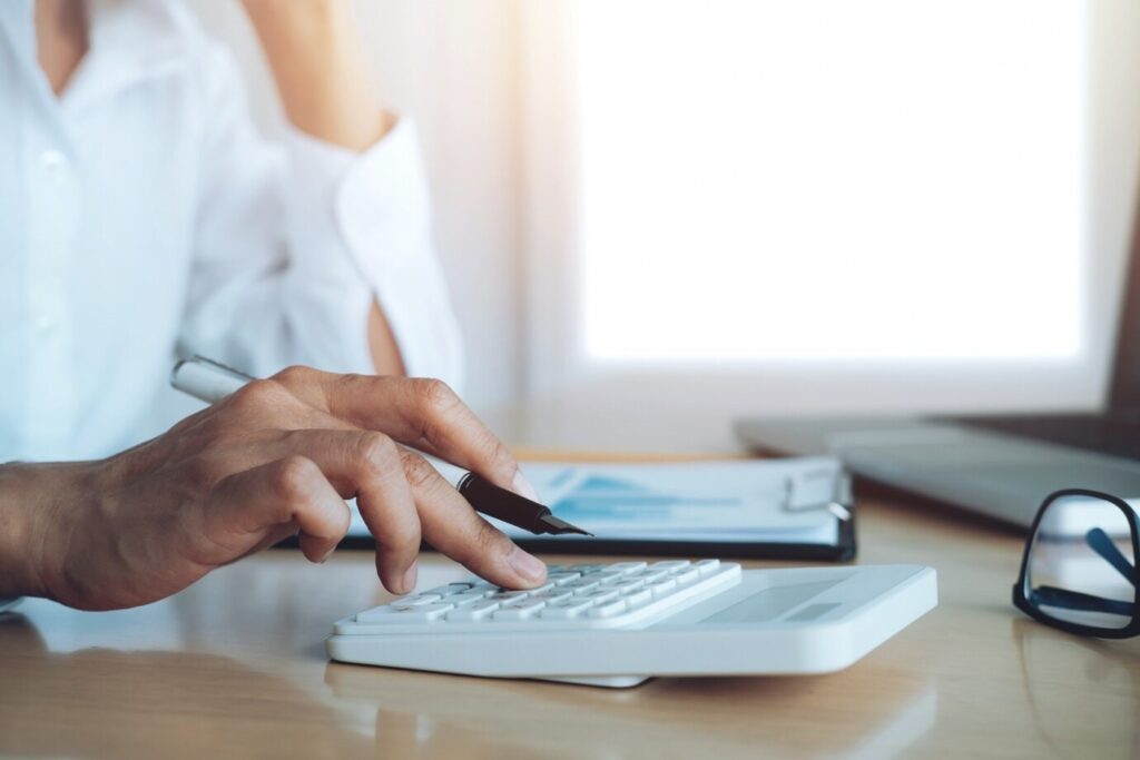 A man calculating expenses on a white calculator, representing the importance of budgeting to achieve stress-free home expansion planning.