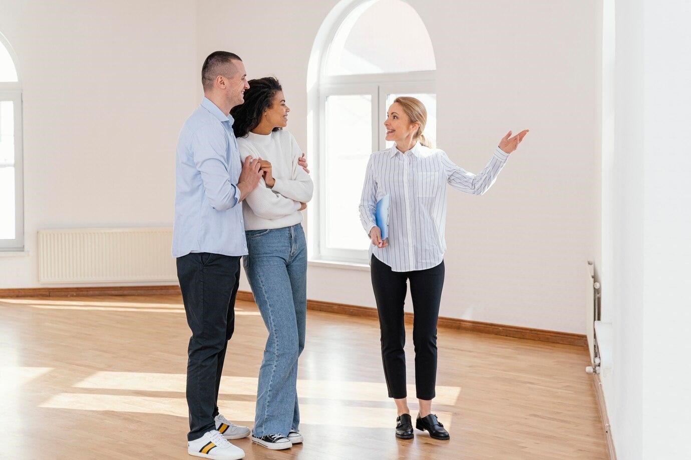 A smiling realtor shows a house to a young couple, representing the importance of knowing how to flip houses.