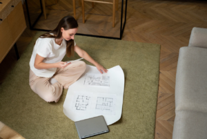 A young woman sitting on the floor holding the floor plans of her house, representing the importance of stress-free home expansion planning.