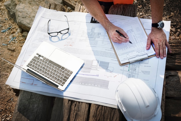 Construction contractor on a building site checking commercial construction permits with a clipboard and a laptop.